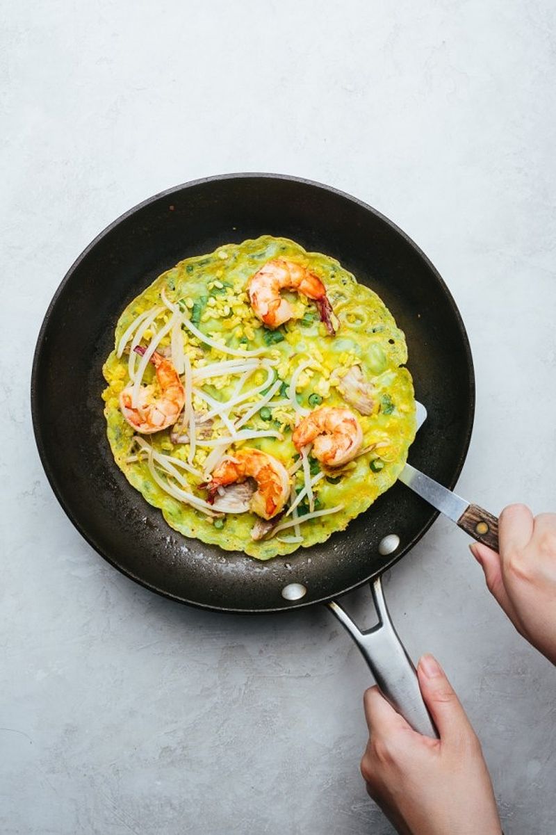 A pan with cooked crepe and another hand with a spatula underneath the crepe