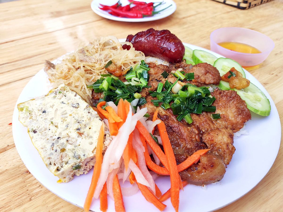 A plate of com tam featuring grilled pork, egg meatloaf, and condiments.