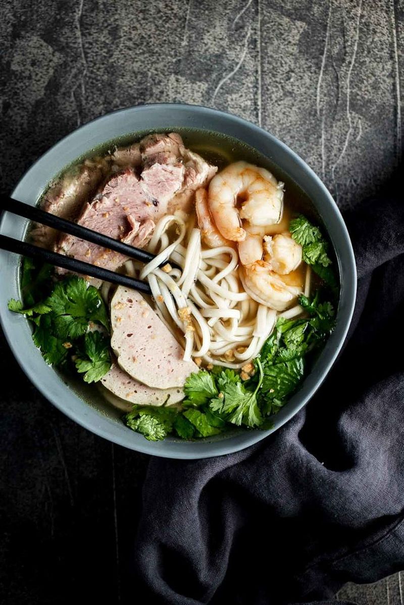 Banh Canh garnished with fresh herbs and lime