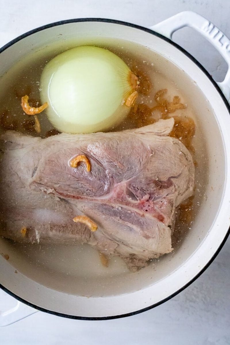 Pork shoulder, dried shrimp, and onion prepared for the broth in a white pot