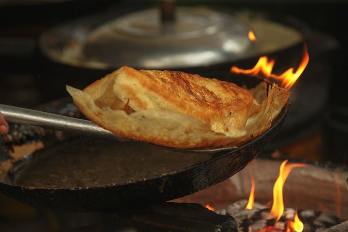 A man cooking banh xeo in a hot pan, highlighting the sizzling process