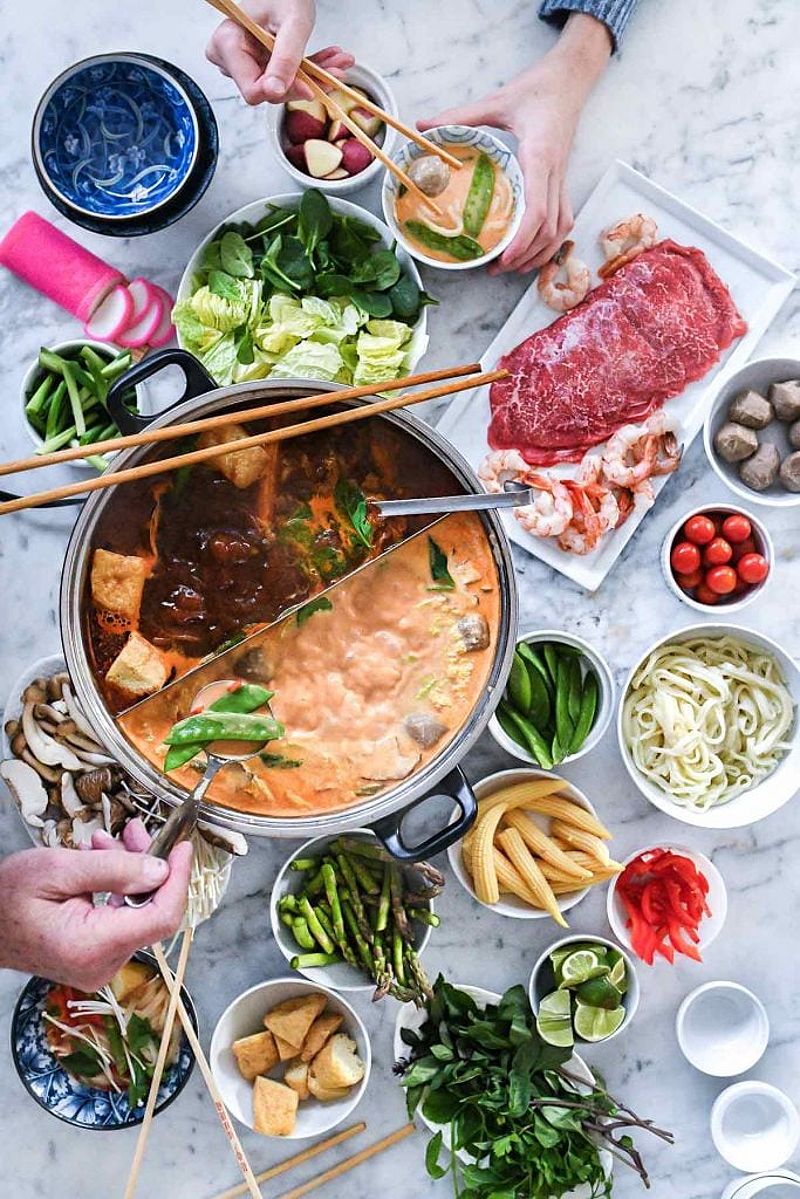 Assortment of hot pot broths, vegetables, and proteins on marble counter