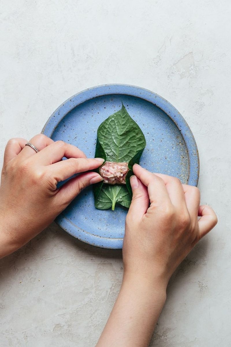 Hands folding betel leaf over beef filling