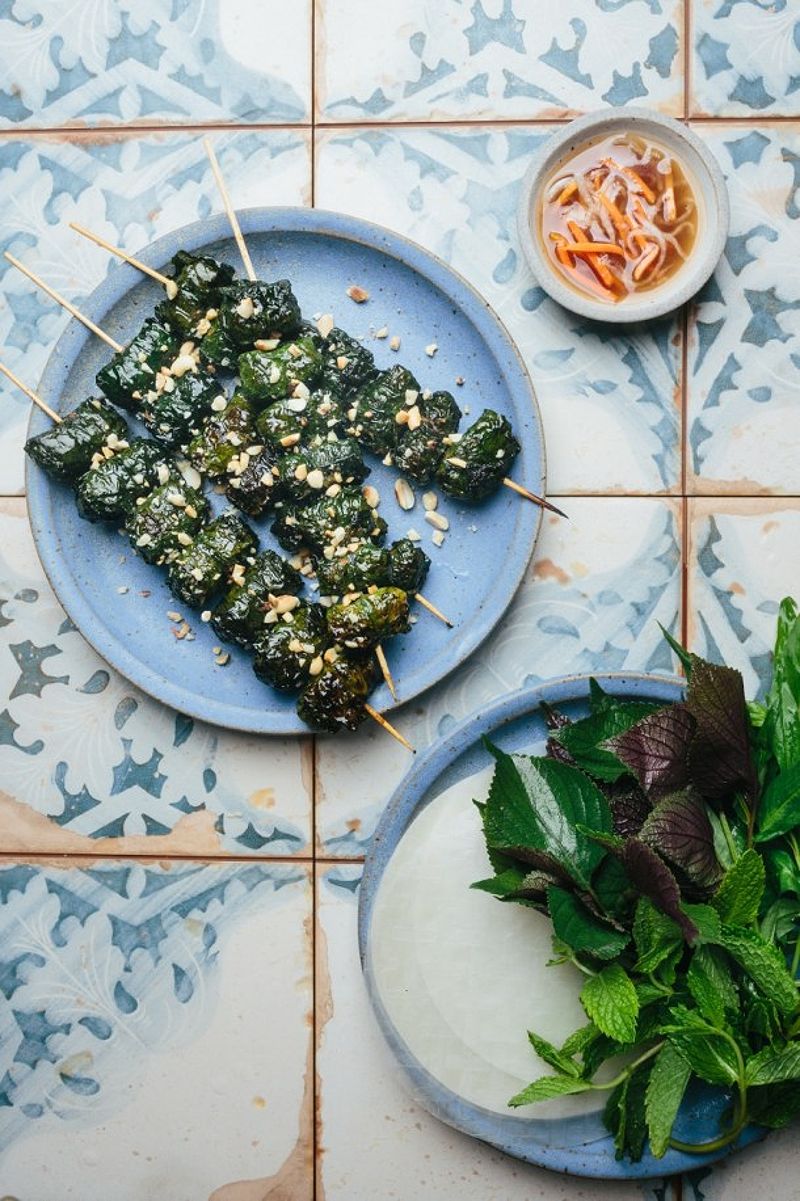 Plate with grilled beef skewers, dipping sauce, rice paper, and herbs