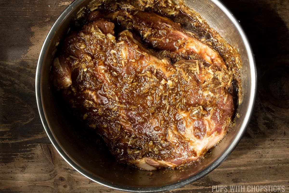 Pork shoulder slathered in lemongrass marinade in a metal bowl