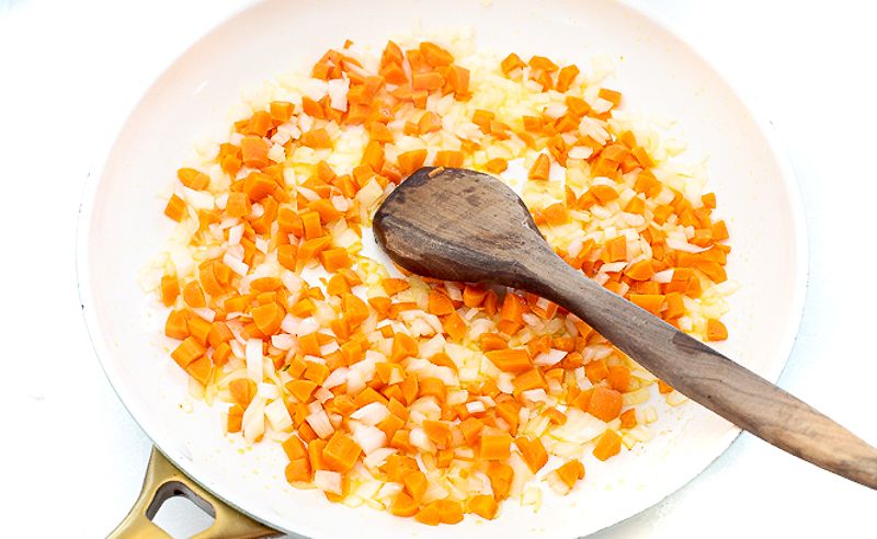 Sautéing diced carrots and onions in large skillet